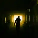 Ciemna, oświetlona korytarz z sylwetą postaci w mroku, symbolizujący horror gry